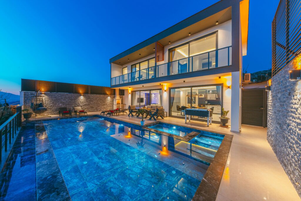 Modern luxury villa at dusk with an illuminated swimming pool and elegant terraces.