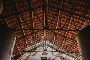 View of architectural wooden roof trusses inside an old factory with exposed ceiling and natural light.