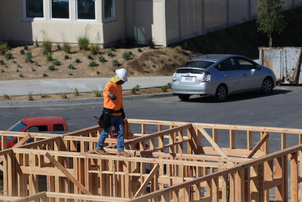 A construction worker wearing safety gear walks on wooden framing at a construction site.