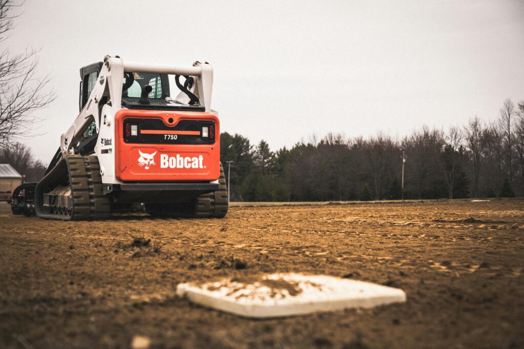 A skid loader working on maintaining a baseball field under construction.