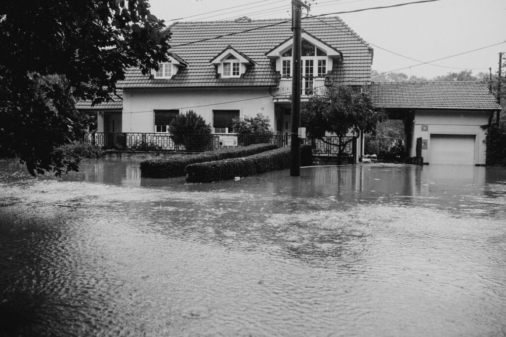 A black and white image showing a suburban house surrounded by floodwater.