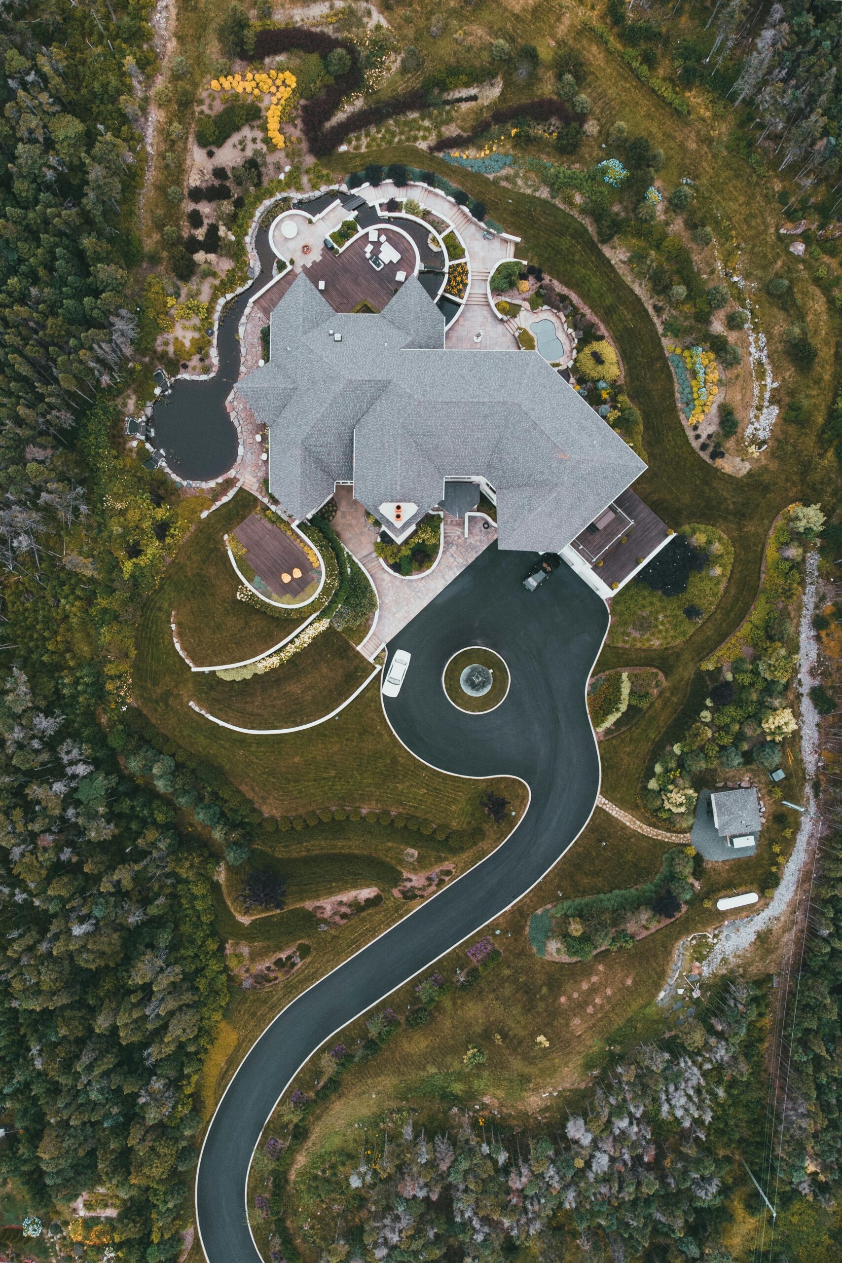 Drone shot of a modern mansion with landscaped gardens and winding driveway.  Do Your Deck Ohio LLC performs residential construction 